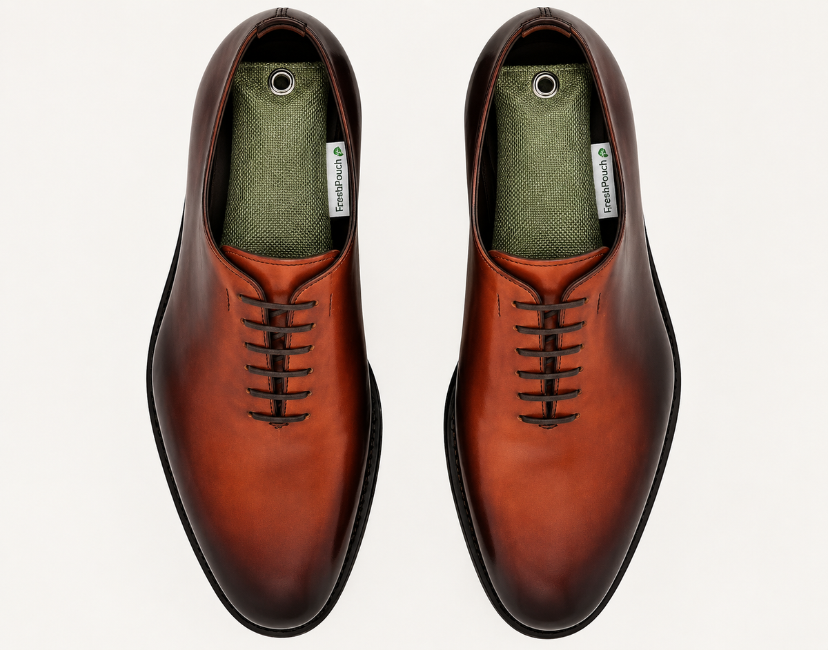 A pair of men's brown leather lace-up dress shoes shown from a top-down view on a light off-white background. The shoes feature a gradient brown finish, dark brown laces, and a green fabric lining with a visible 'FreshPouch' brand tag.