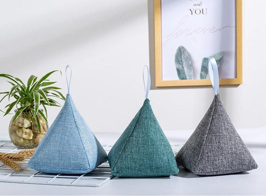 Three pyramid-shaped fabric baskets in blue, green, and gray on a white surface with a plant and framed picture in the background.